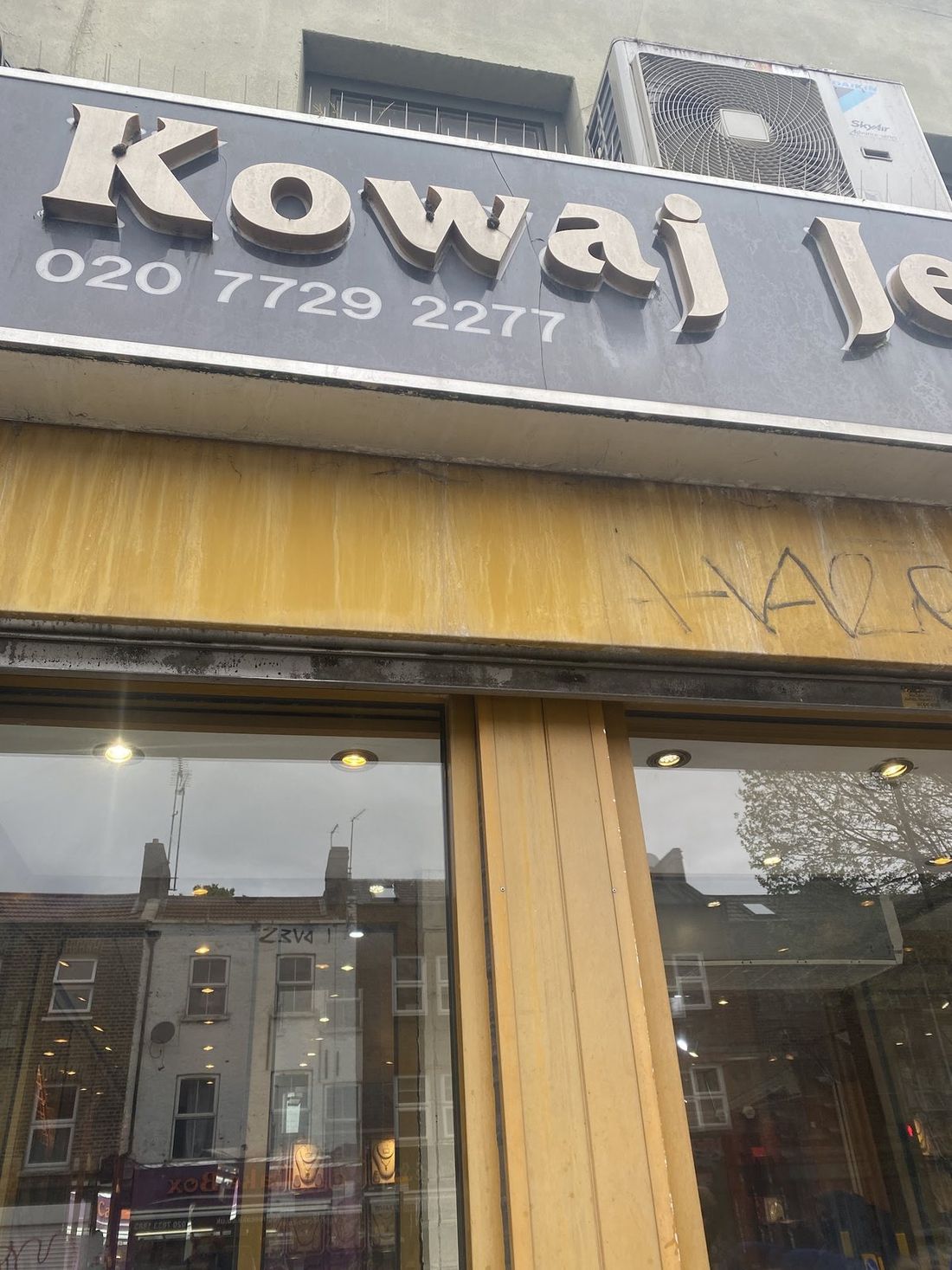 The shopfront sign of Kowaj Jewellers on Bethnal Green Road, gold lettering on a grey fascia above the display window